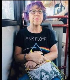 a woman with purple hair sitting on a bus wearing a pink floyd t - shirt