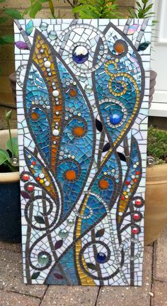 a blue and yellow mosaic art piece sitting next to a potted plant