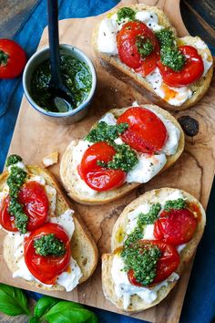 four pieces of bread with tomatoes, cheese and pesto on them sitting on a cutting board