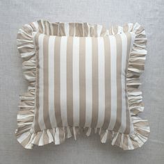 a striped pillow with ruffled edges on a gray background in front of a white wall