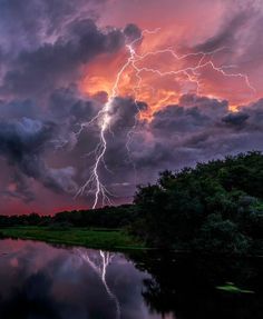 a large cloud filled with lots of lightning next to a body of water under a cloudy sky