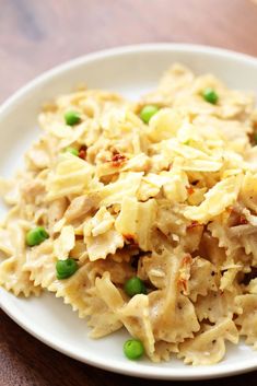 a white plate topped with macaroni and peas on top of a wooden table