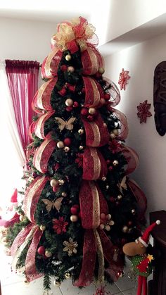 a decorated christmas tree with red and gold ribbons on it's top, in front of a window