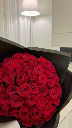 a large bouquet of red roses in a black paper wrapper on a white table