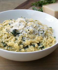 a pasta dish with spinach and cheese in a white bowl on a wooden table