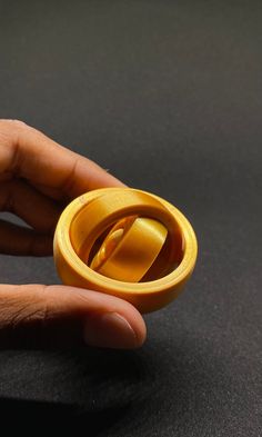 a hand holding a yellow ring on top of a black surface with one finger in it