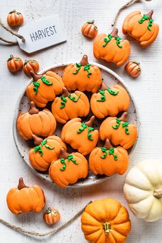 small pumpkins are sitting on a plate next to some smaller ones with green leaves