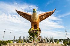 a large golden bird statue sitting on top of a lush green field next to a blue sky