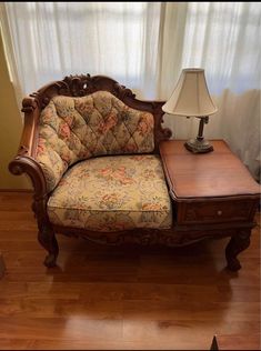 a chair and table with a lamp on it in front of a curtained window