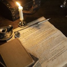 an old document with a lit candle on it next to a pen and inkwell