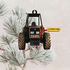 a tractor ornament hanging from a pine tree with a name tag on it