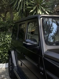 a black mercedes g class parked in front of a house with trees and bushes behind it