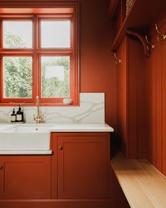 a kitchen with red walls and white counter tops, along with a sink in front of a window