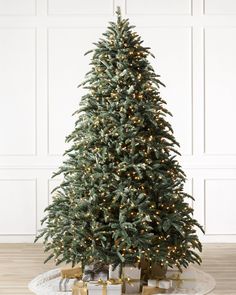 a christmas tree with lights and presents on the floor in front of a white wall