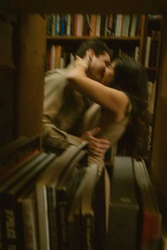 a man and woman are kissing in front of bookshelves with their arms around each other