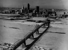 an old photo of a bridge in the middle of a city with tall buildings behind it