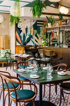 an empty restaurant with green chairs and plants hanging from the ceiling, along with tables set for four