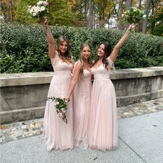 three bridesmaids in pink dresses posing for the camera with their bouquets up