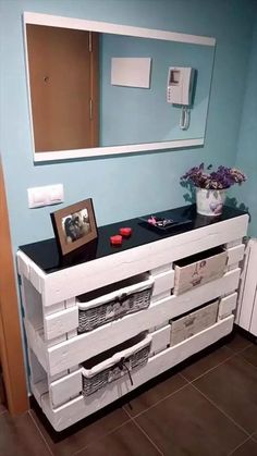 a white dresser with drawers and pictures on the top, in a blue walled room