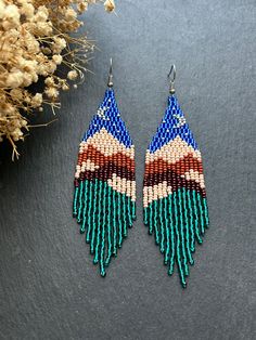 Beaded earrings featuring a landscape depicting mountains and the moon. The upper part of the earrings is in blue, representing the night sky with the moon, gradually transitioning into beige and brown, symbolizing the mountains. The lower part is adorned with fringe made of green beads, imitating a forest. These landscape earrings will create a stylish and expressive accent in your look. Perfect for those who love unique and colorful accessories. Made from Czech beads. Hypoallergenic clasp. Len Artisan Blue Earrings With Dangling Beads, Artisan Blue Beaded Earrings, Artisan Blue Beaded Earrings With Colorful Beads, Unique Blue Earrings With Colorful Beads, Artisan Blue Drop Earrings, Artisan Blue Round Beaded Earrings, Unique Blue Beaded Earrings With Round Beads, Blue Earrings With Dangling Beads, Unique Blue Earrings With Dangling Beads