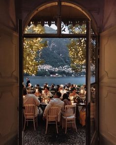 people are sitting at tables in front of an open window with lights on the outside