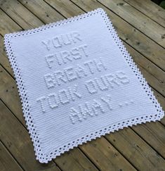 a white crocheted square with words written on it sitting on a wooden surface