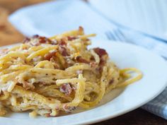 a white plate topped with pasta covered in cheese and bacon next to a blue dish towel