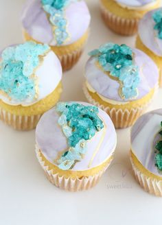 cupcakes with blue frosting and green sprinkles on white surface