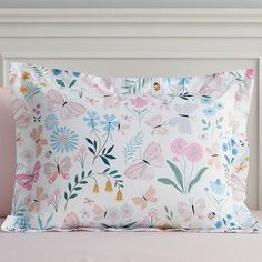 a white pillow with pink, blue and yellow flowers on it sitting on a bed