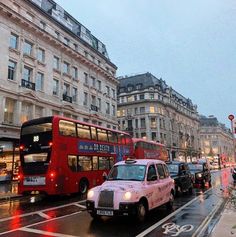 a red double decker bus driving down a street next to tall buildings on a rainy day