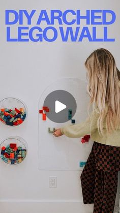 a woman standing in front of a white wall with legos on it's side