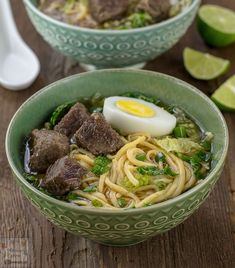 two bowls filled with noodles, meat and broccoli on top of a wooden table