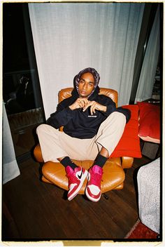 a woman sitting in a chair with her legs crossed and wearing red shoes, looking at the camera