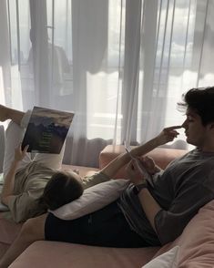 two people are laying on a couch reading books while one person is lying down with his feet up