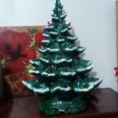 a green ceramic christmas tree sitting on top of a wooden table next to a painting