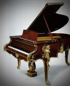 a grand piano with gold decorations on the body and sides, sitting upright against a white background