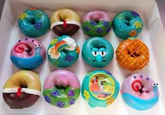 an open box filled with donuts covered in different colored frosting toppings and designs