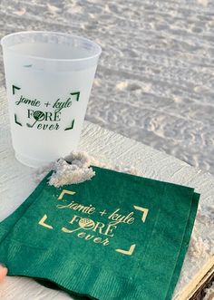 a cup and napkin sitting on top of a table next to the ocean in front of some sand