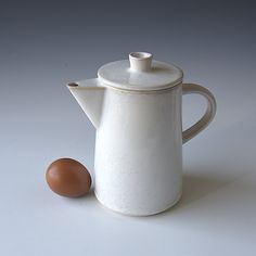 an egg sitting next to a white tea pot