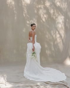 a woman in a white dress is standing with her back turned to the camera and holding a bouquet