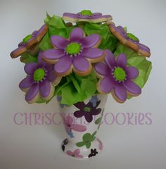 purple flowers are in a white vase with green leaves and cookies on the rims