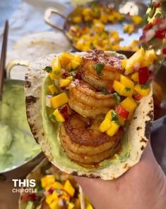 a person holding up a taco filled with shrimp and mango salsa