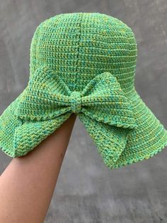 a woman's hand wearing a green knitted hat with a bow on it