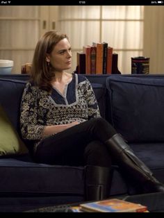 a woman sitting on top of a blue couch in front of a book shelf filled with books