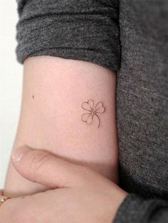 a small four leaf clover tattoo on the left wrist and right hand behind her arm