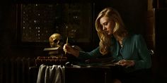 a woman sitting at a desk writing in front of a skull