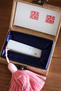 an open box with some pink tassels and a white object in it on a wooden table