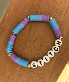 a beaded bracelet with the word stitch spelled out in white and blue beads on a wooden table