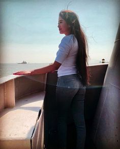 a woman standing on the side of a boat looking out at the ocean with her long hair blowing in the wind