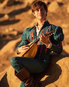 a man sitting on top of a rock while holding a ukulele in his hands